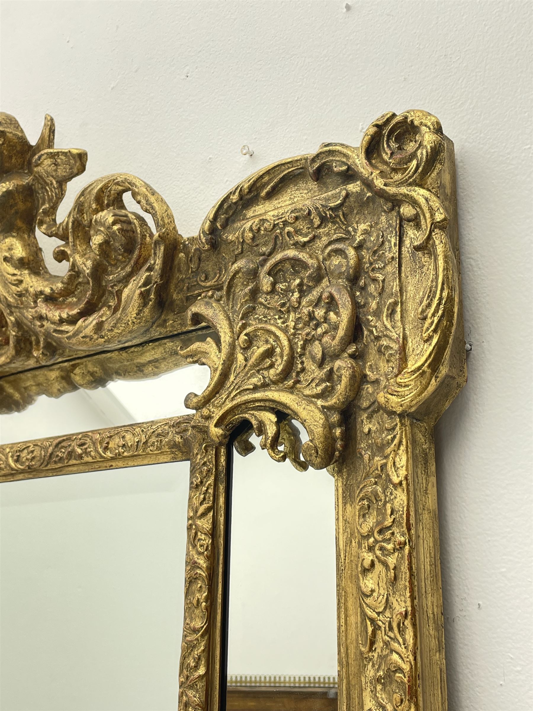 Large Victorian style gilt cushion framed mirror, putti holding urn with scrolled foliage pediment above central rectangular bevelled plate, the frame decorated with moulded foliate, each corner set with ornate cartouche