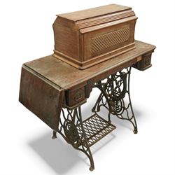 Early 20th century Singer treadle sewing machine, the black enamel machine with gilt floral and scroll transferwork set within a timber cabinet top with folding leaf, raised on cast-iron base with pierced geometric treadle and 'Singer' name stretcher, flanked by two small drawers
