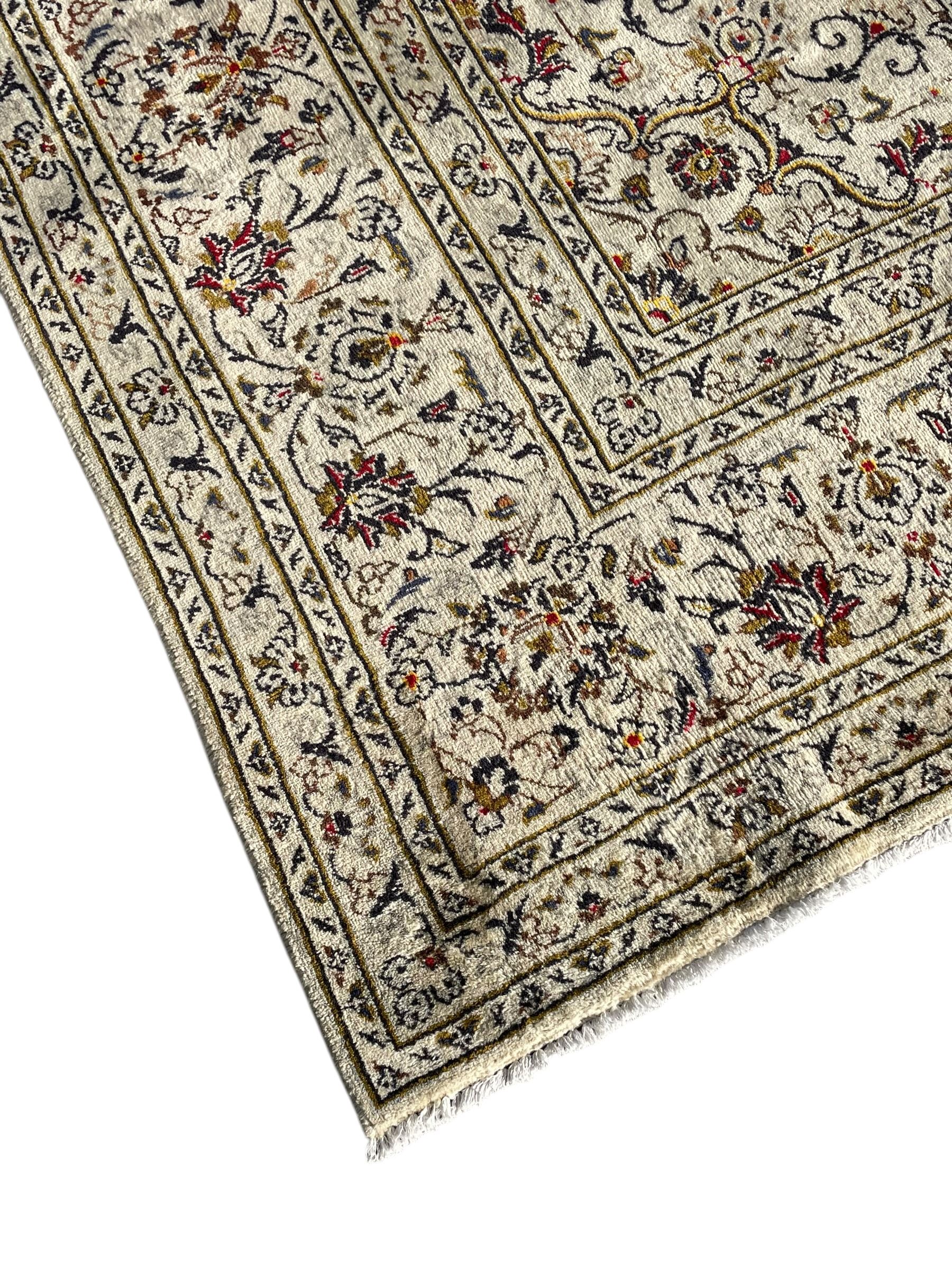 Persian Kashan ivory ground carpet, central medallion decorated with sixteen arranged palmette motifs, within a field decorated with swirling leafy branches and stylised plant motifs, the main border decorated with matching swirling pattern, within floral pattern guard stripes 