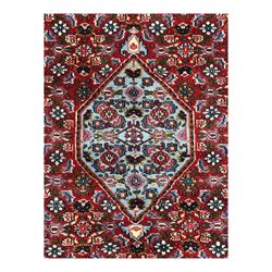 Persian crimson ground rug, central light blue lozenge medallion with floral motifs, the densely decorated crimson field filled with repeating flower heads and trailing leafy vines, the black and red border with interlacing foliate patterns and floral cartouches, surrounded by guard stripes