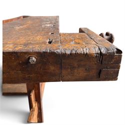 Large early 20th century rustic stained reclaimed pine workbench, the substantial plank top with recessed tool well and two homemade wooden screw vices, above a single frieze drawer and slatted undertier, raised on trestle end supports