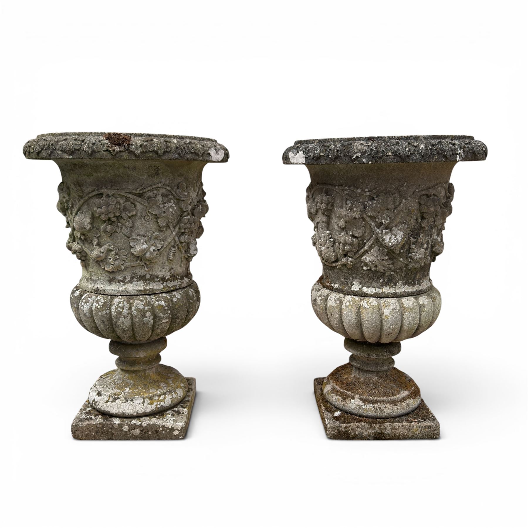 Pair of quality antique weathered three-piece composite stone garden urns, the flared rim moulded with repeating acanthus leaves, over a deep-relief campana body decorated with fruiting grapevines and ivy leaves, the gadrooned underbelly over a turned socle and square base