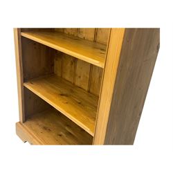 Early 20th century pine bookcase, projecting cornice over arched open shelving area with five adjustable shelves, on shaped plinth base