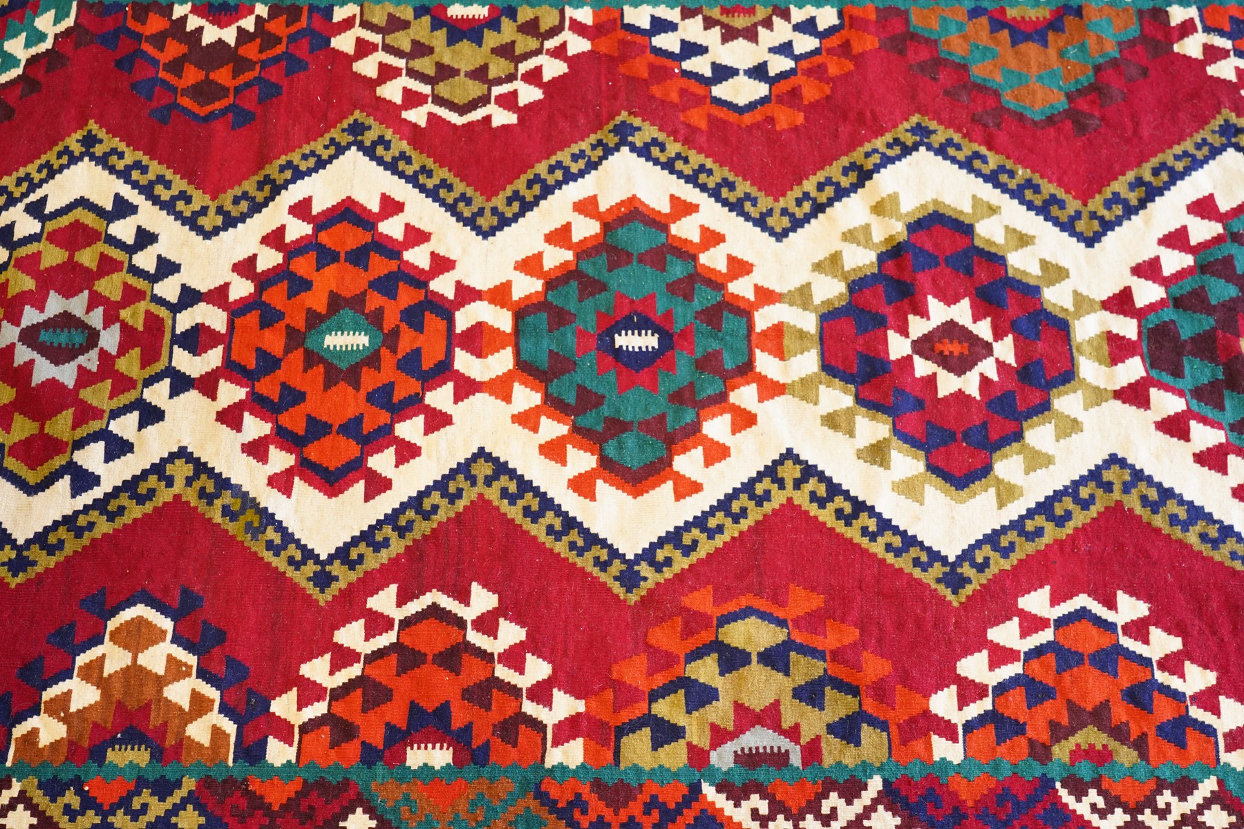 Persian Qashqai crimson ground rug, the central narrow ivory field decorated with repeating hooked geometric lozenges in multicolours, with a densely decorated guard band