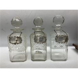 Edwardian oak three bottle tantalus, with brass mounts and three square sided cut glass decanters each with hallmarked silver decanter labels, complete with key, H31cm
