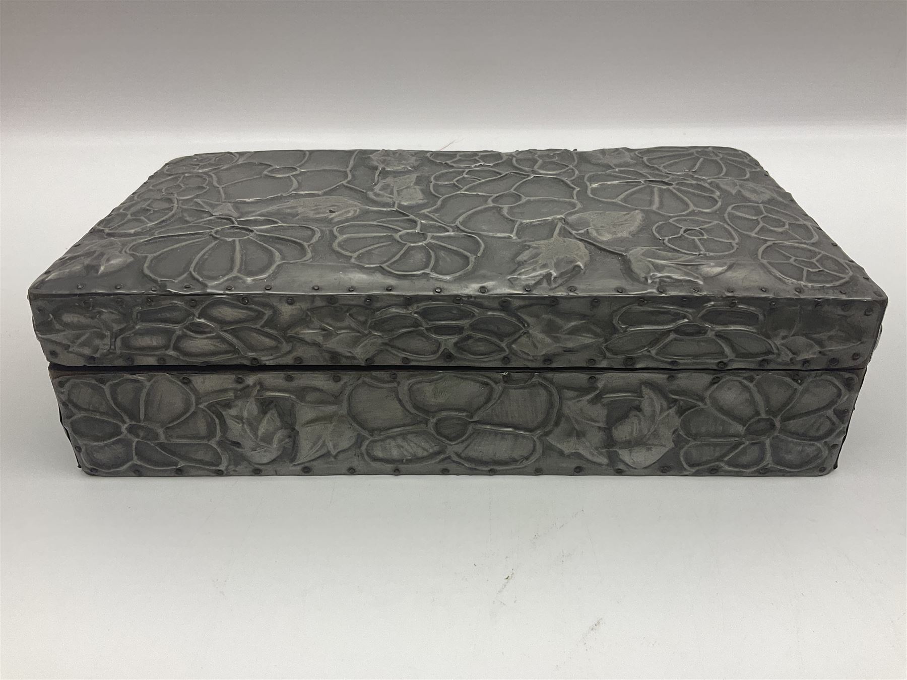 Liberty & Co Tudric pewter cigarette box, of plain rectangular form, with planished decoration to the slightly domed cover, opening to reveal a softwood interior, stamped Made in England 01234 Tudric Solkets beneath, together with another cigarette box, with applied pewter panels repousse decorated throughout with flower heads and leaves, with compartmentalised softwood interior, largest H5.5cm, W23cm