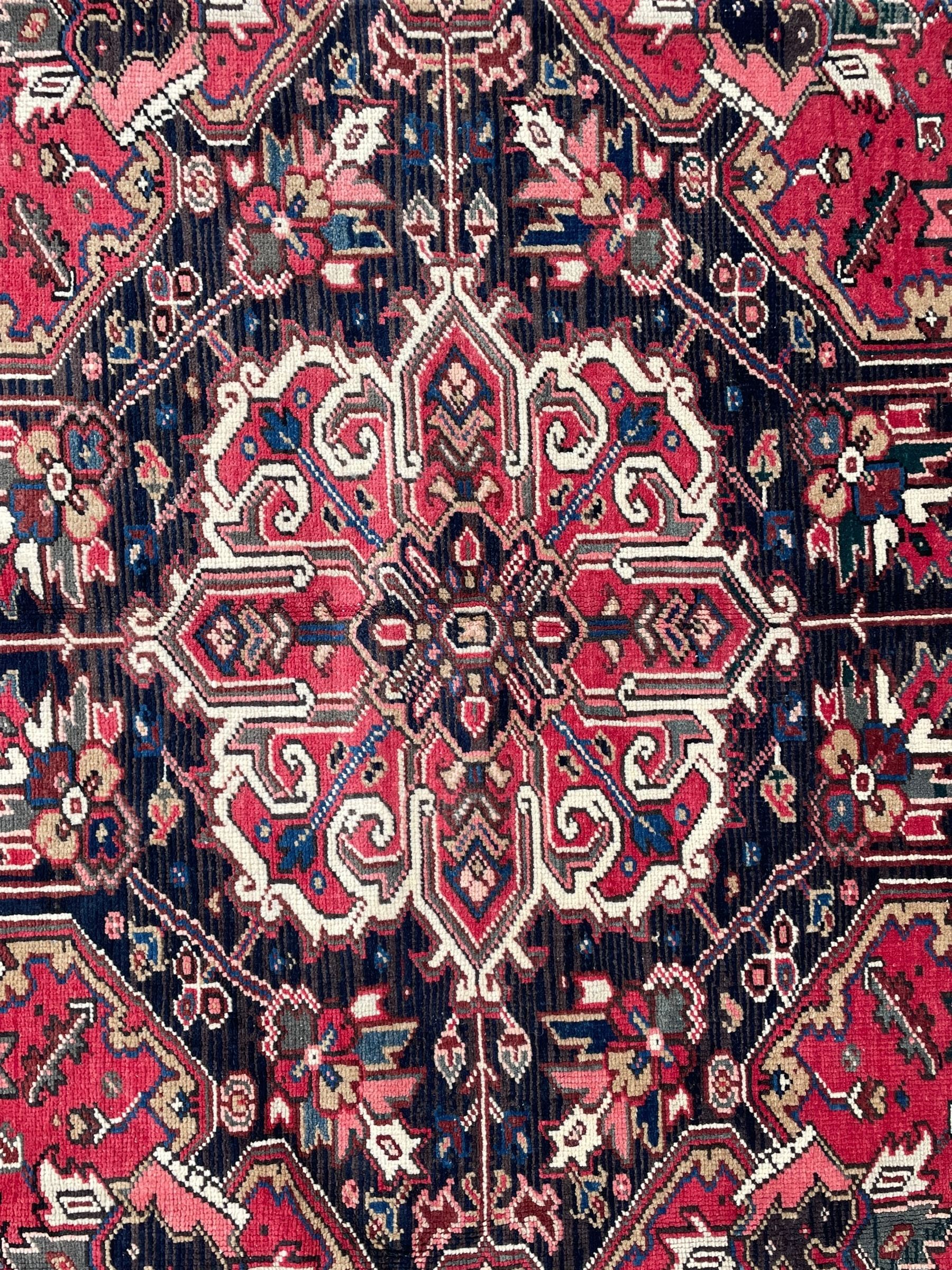Persian Heriz red ground rug, central scrolled medallion on dark ground decorated with floral motifs, the surrounding field decorated with stylised plant motifs and smaller geometric symbols, guarded border with repeating pattern punctuated with rosettes and flower heads 