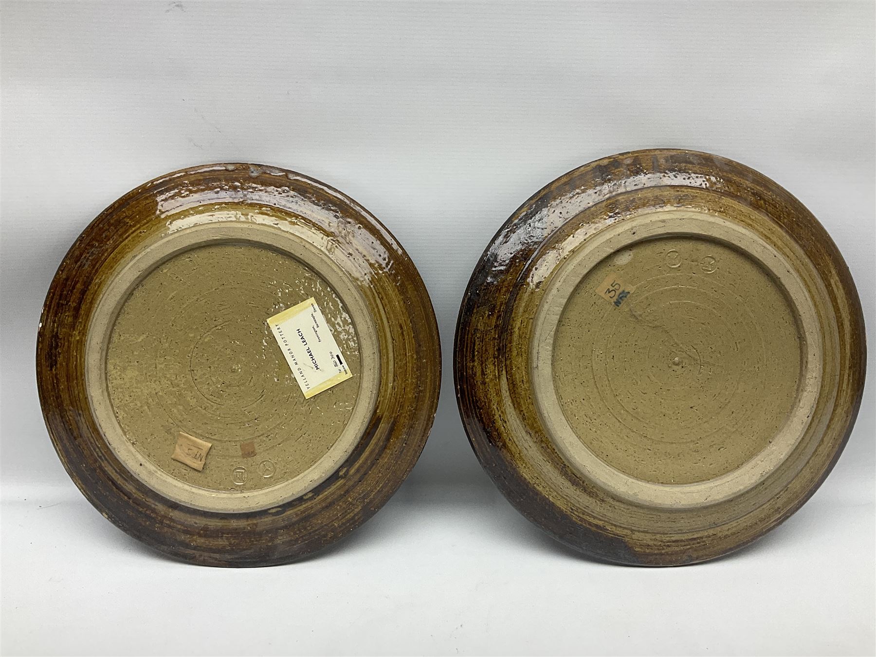 Michael Leach (British 1913-1985) for Yelland pottery; two large glazed stoneware plates with dark brown stylised decoration upon oatmeal ground, together with a jug in merging blue, green and brown, all with impressed marks beneath, largest plate D37cm