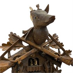 A large and imposing 20th century three train 30hr cuckoo clock with automata and musical features, profusely carved case with a carousel, animals, leaves and sporting guns, dial with pierced wooden numerals and wooden hands, with three weights and pendulum, strike/silent facility. 
