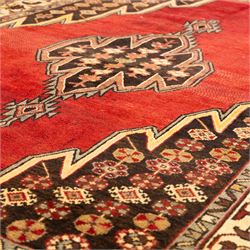 West Persian Mazlaghan hand-knotted rug, madder red field with central stepped lozenge medallion with pendant motifs flanked by angular serrated spandrels filled with small geometric devices, enclosed within multiple borders featuring stylized floral and geometric motifs, with cotton fringe ends 