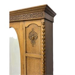 Early 20th century oak wardrobe, projecting cornice of blind fret-work frieze, oval bevel edge mirror door, half spiral turned pilasters, drawer to base with mouldings, on turned bun feet