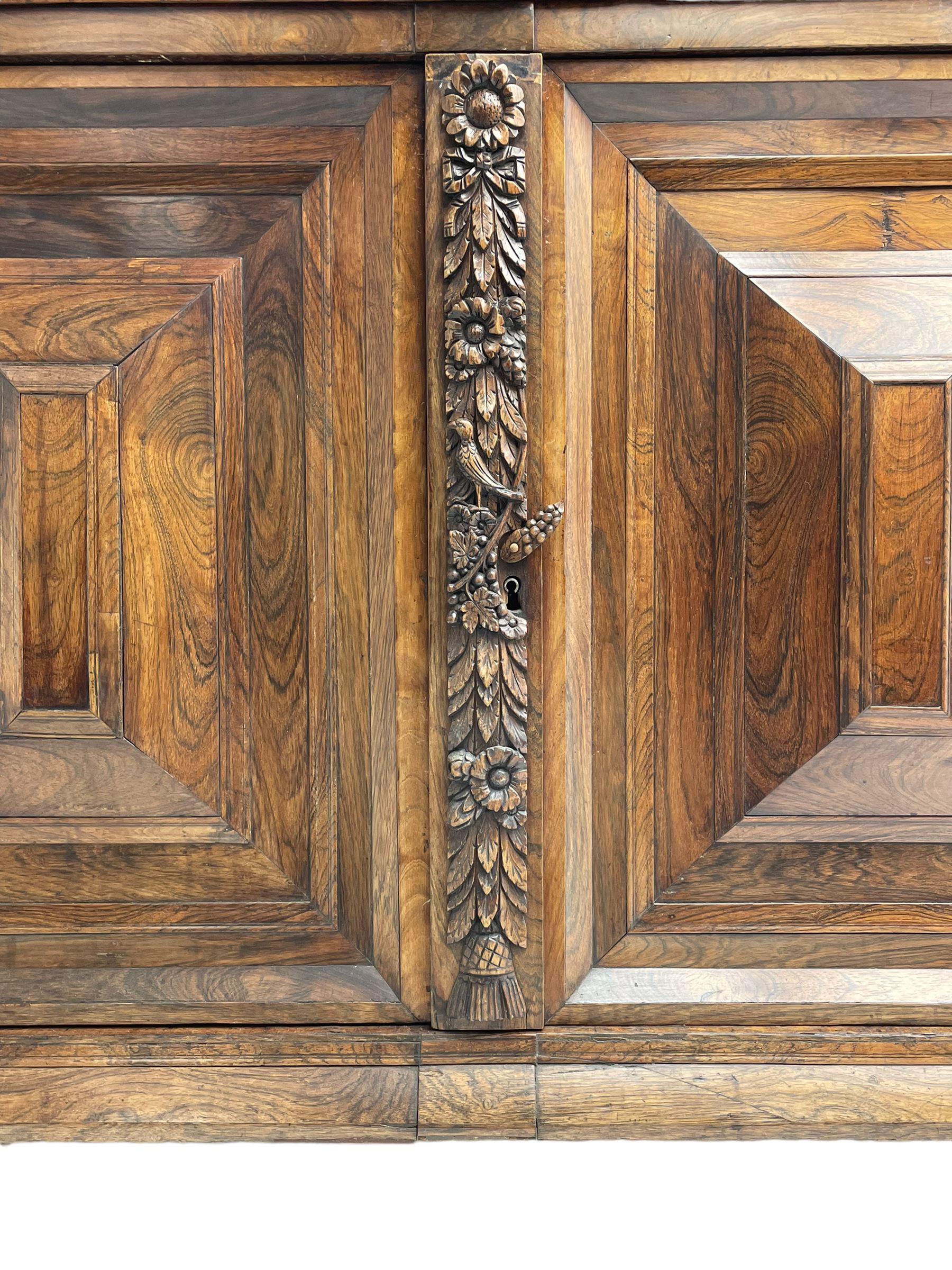 Late 17th century Flemish/Dutch rosewood and oak ‘Zeeuwse Kast’ or cupboard, projecting cornice carved with three putti masks, the uprights carved with lion masks over ribbons, flower heads and foliage, enclosed by four geometric panelled doors, lower central upright carved with flower head over foliate ribbon with bird among foliage, the escutcheon hidden by swivel berry carved cover, interior fitted with shelves, two drawers and shallow hinged cupboard, on two large turned and ebonised feet, circa 1680