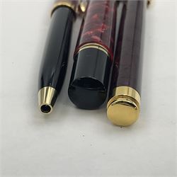 Pelikan Souveran Ruby Red fountain pen, the marbled resin barrel and cap with gilt beak shaped clip and double cap band with gold bi-colour nib stamped 14C-585 M, together with matching ballpoint, Pelikan New Classic fountain pen with marbled maroon barrel and gold nib stamped 14C-585 B, largest L13.5cm (3)
