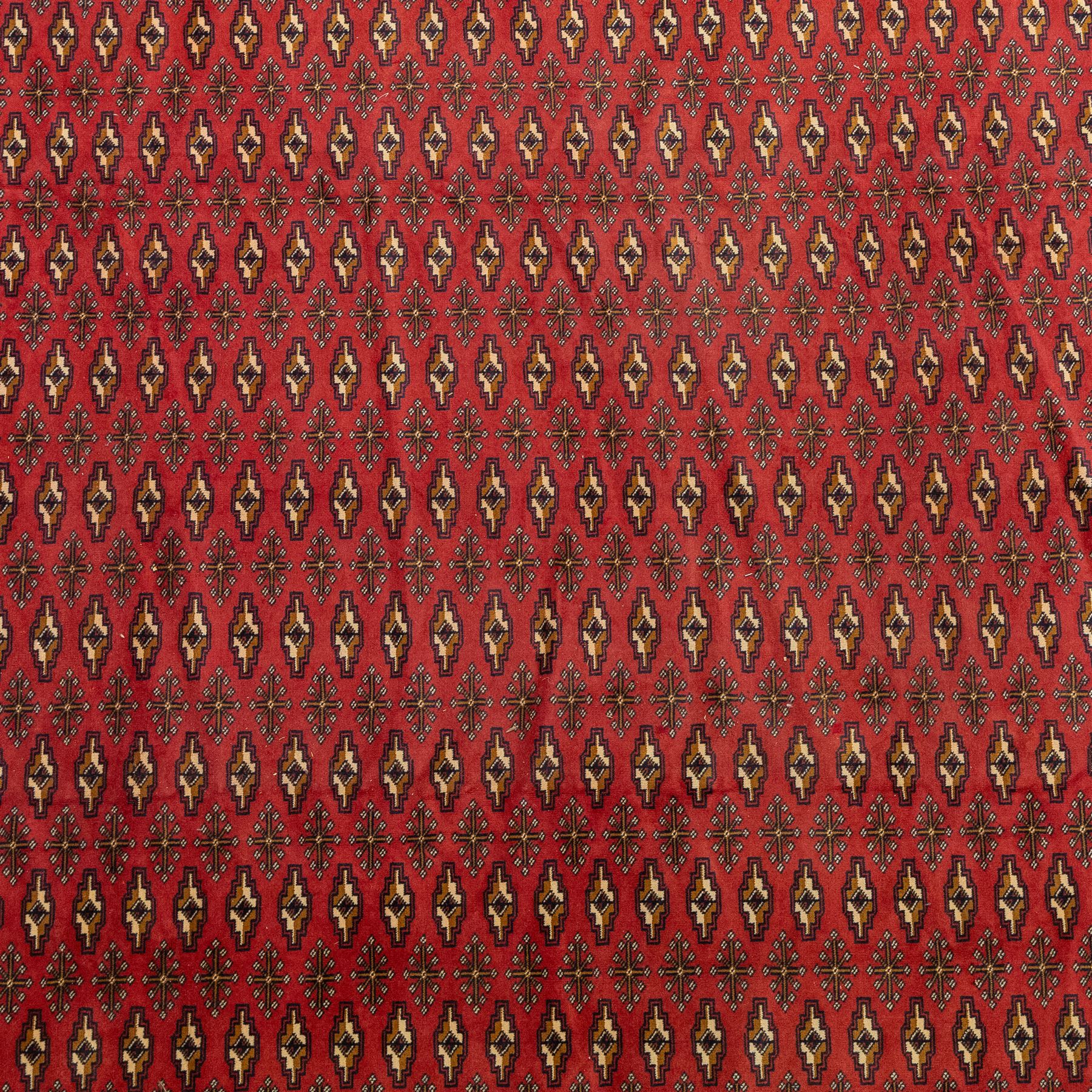 North East Persian Turkoman hand-knotted carpet, madder red field decorated with rows of repeating Tekke guls, in offset horizontal bands and interspersed cruciform subsidiary motifs, enclosed within narrow geometric borders featuring stylized tribal devices, with fringe ends   