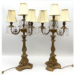 A pair of large gilt table lamps, the foliate and palmette detailed column supporting three curved branches and a central fitting, each supporting clear droppers, and cream shades, upon a trefoil base, H88cm.  