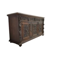 Victorian heavily carved oak sideboard, the moulded top carved with foliate decoration to the edge, fitted with two drawers and three cupboards, the drawer fronts carved with green man mask handles and scrolling foliage, the panelled doors carved with interlacing foliage, on turned compressed bun feet