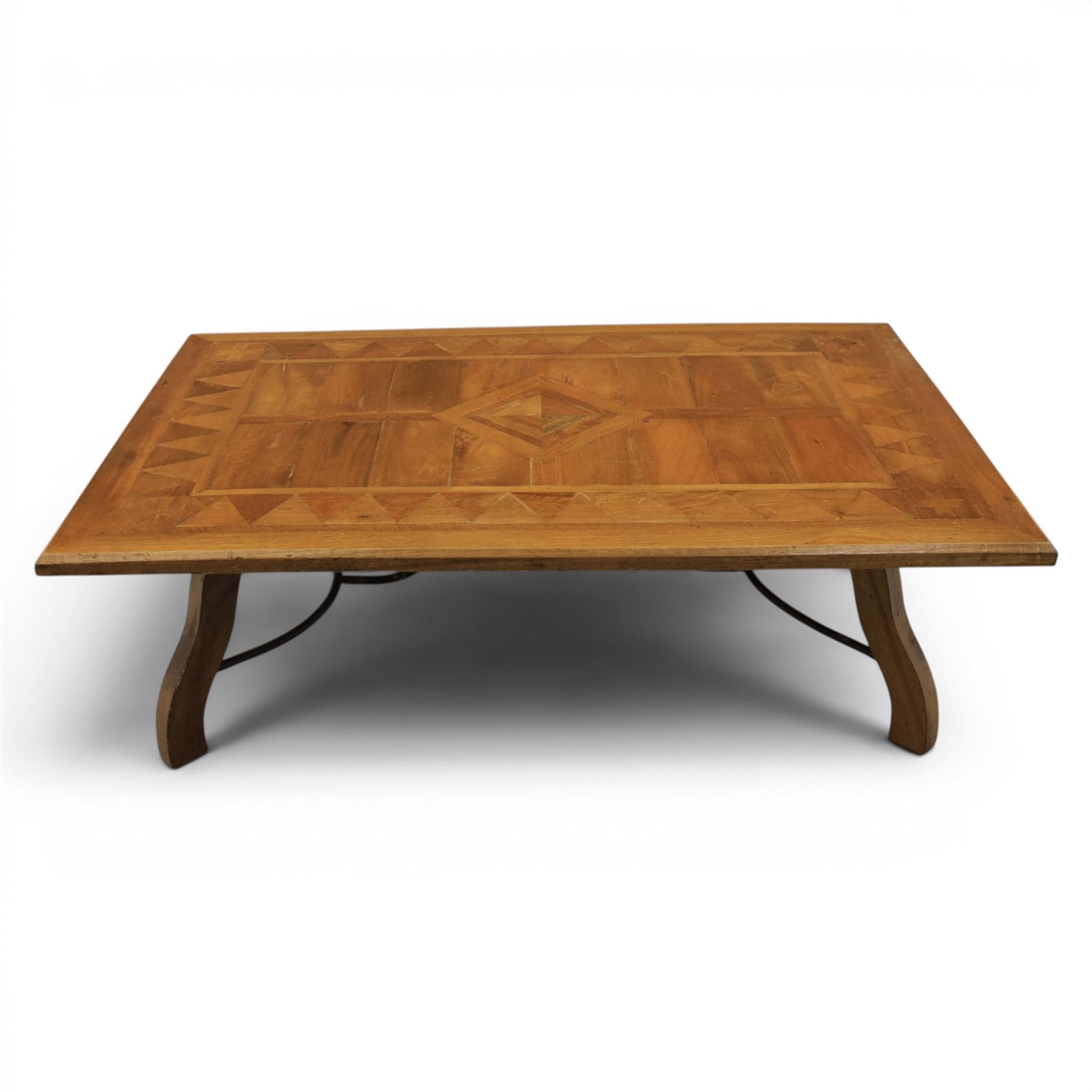 20th century Spanish design oak coffee table, rectangular parquetry top with geometric star and triangular inlaid decoration, moulded edge, on shaped trestle end supports united by black painted wrought iron scroll stretchers