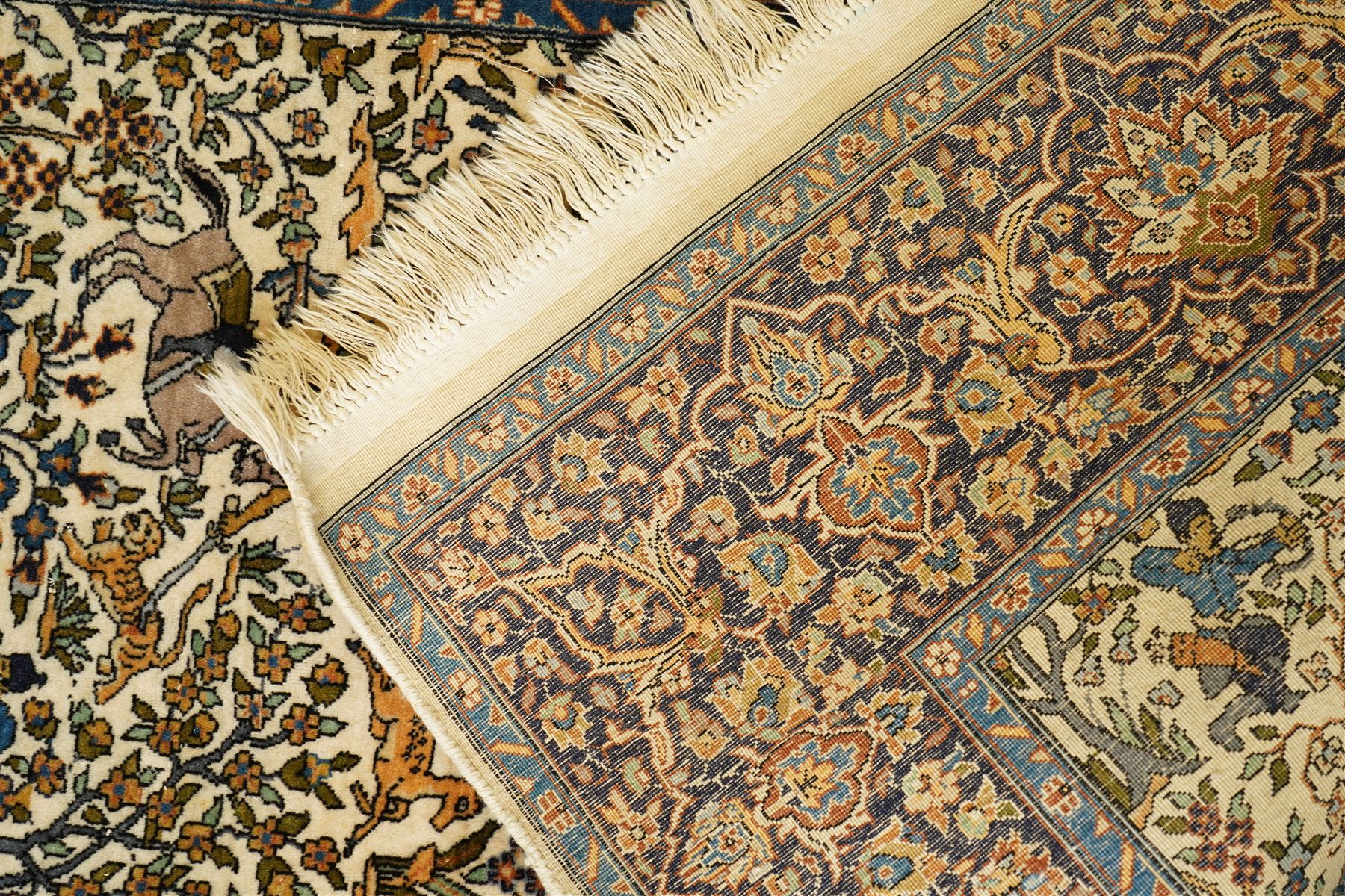 Persian pictorial rug featuring a hunting scene, ivory field with mounted hunters, animals, birds and trees, rich navy and terracotta floral border with rosettes and palmettes 