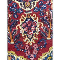 Mid-20th century Persian ground rug, featuring a bold red field and large lobed medallion, flanked by floral corner spandrels, enclosed within multiple borders of stylised vines and palmettes, with fringe to both ends