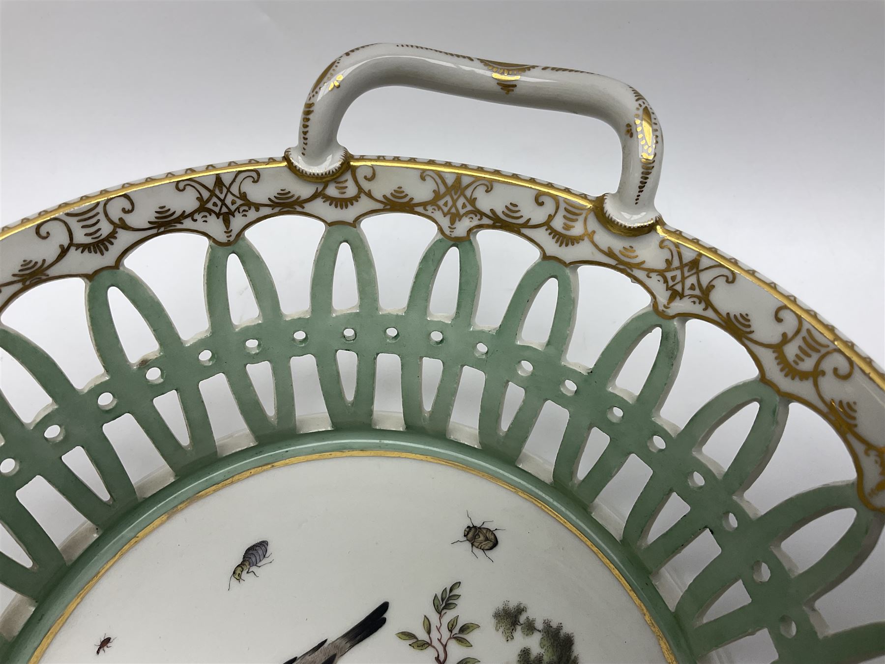 Pair of 19th century German openwork chestnut baskets, with twin handles and scrolling gilt border and star rim, painted to the centre with birds and insects, D22cm 