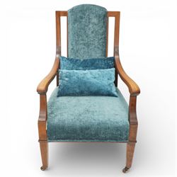 Arts & Crafts mahogany framed armchair, shaped rectangular back with open uprights, padded back, seat and arm supports upholstered in blue velvet, downswept arms on square tapering front supports with brass caps and castors, the rear supports slightly splayed
