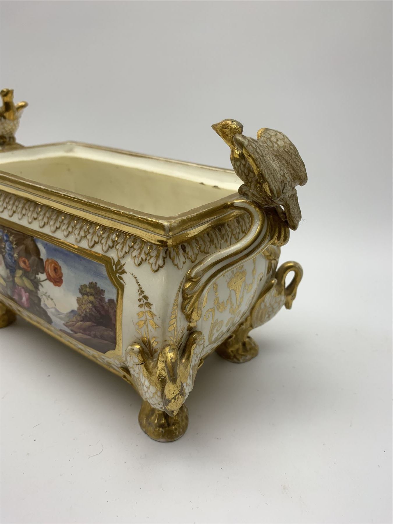 19th century Coalport bough pot, circa 1820, of bombe form, the body with twin handles surmounted by two birds and raised upon four feet modelled as swans, hand painted with two panels depicting an urn of flowers set against a mountainous landscape, the whole heightened in gilt throughout, H13cm L21cm