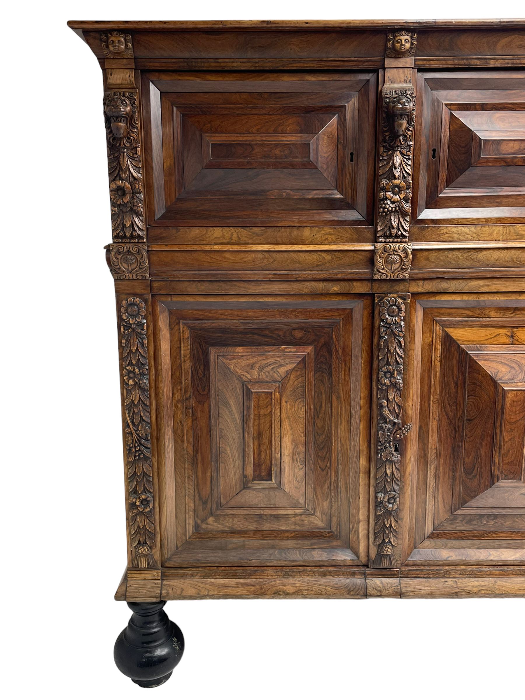 Late 17th century Flemish/Dutch rosewood and oak ‘Zeeuwse Kast’ or cupboard, projecting cornice carved with three putti masks, the uprights carved with lion masks over ribbons, flower heads and foliage, enclosed by four geometric panelled doors, lower central upright carved with flower head over foliate ribbon with bird among foliage, the escutcheon hidden by swivel berry carved cover, interior fitted with shelves, two drawers and shallow hinged cupboard, on two large turned and ebonised feet, circa 1680