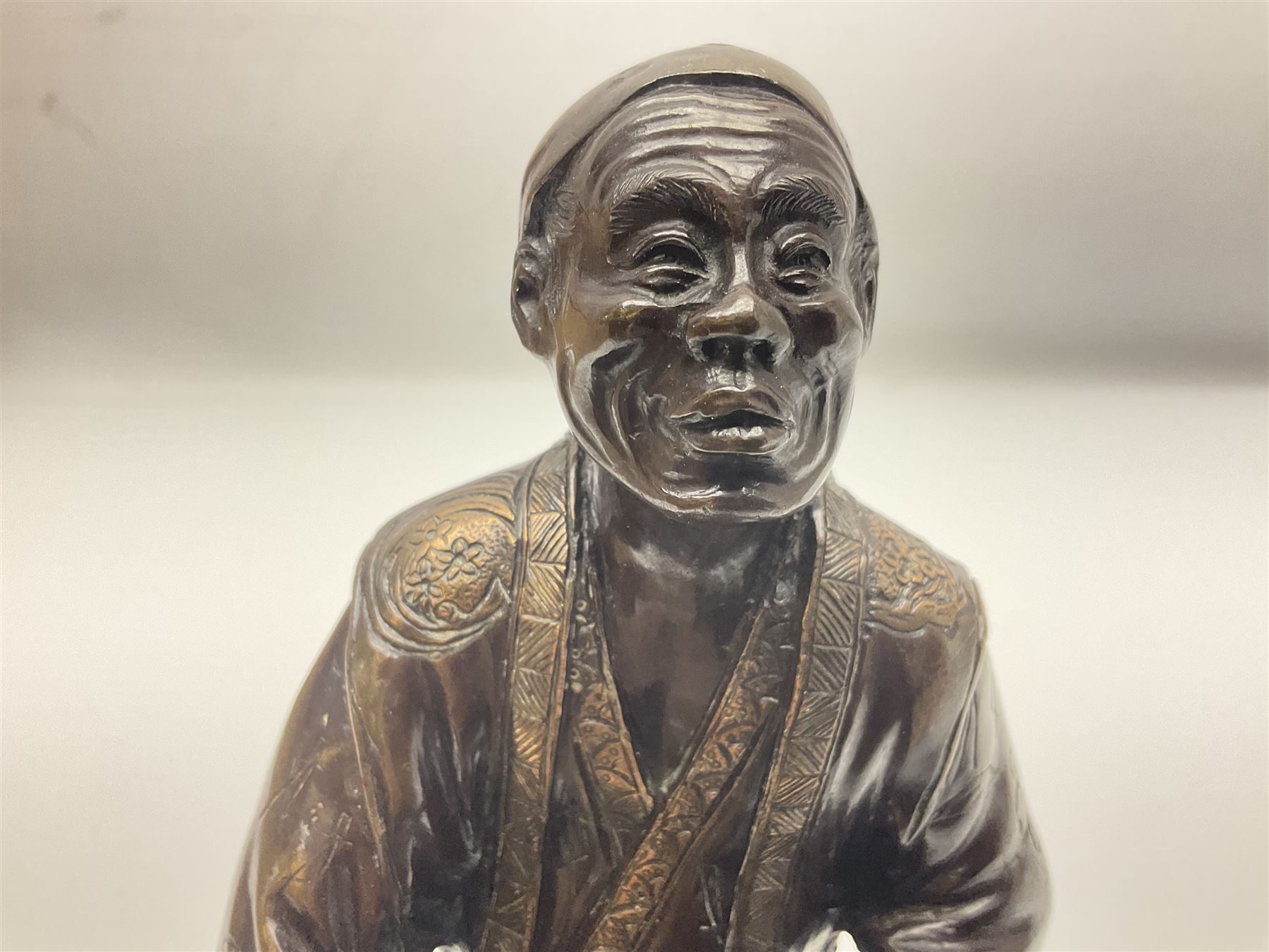 Oriental bronze figure of a gentleman, modelled seated upon barrel with a pipe in one hand and a flask in the other, H21cm