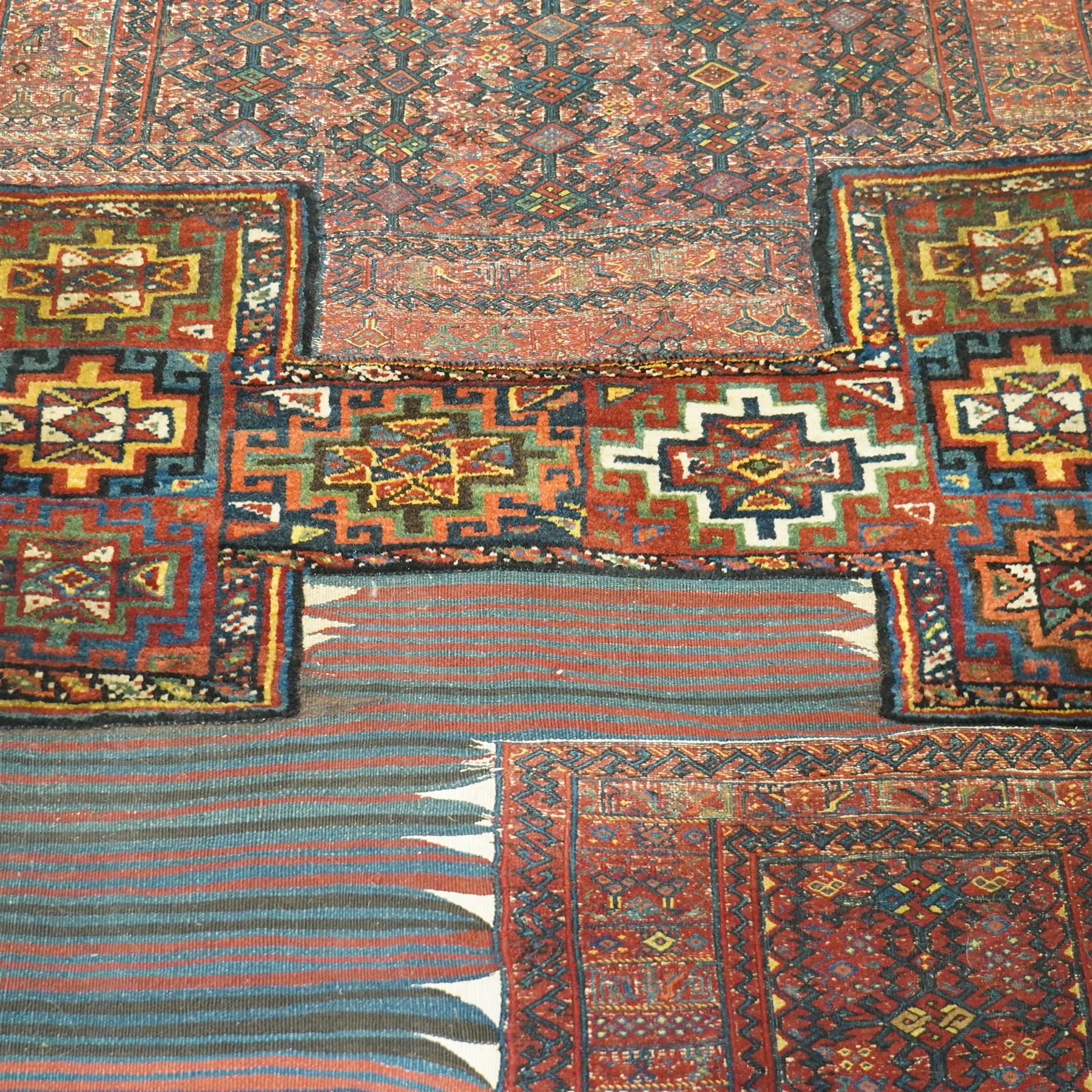 Central Asian vintage saddle cover, probably Turkmen, wool pile and flatweave on wool foundation, decorated with geometric tribal motifs in a palette of madder red, indigo, ivory, and dark brown, with cotton fringe ends 
