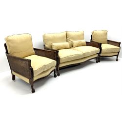 Early 20th century mahogany framed Bergere settee, double cane sides with acanthus carved arms on hairy paw feet, upholstered in a pale gold fabric (W145cm) and two matching armchairs (W66cm)