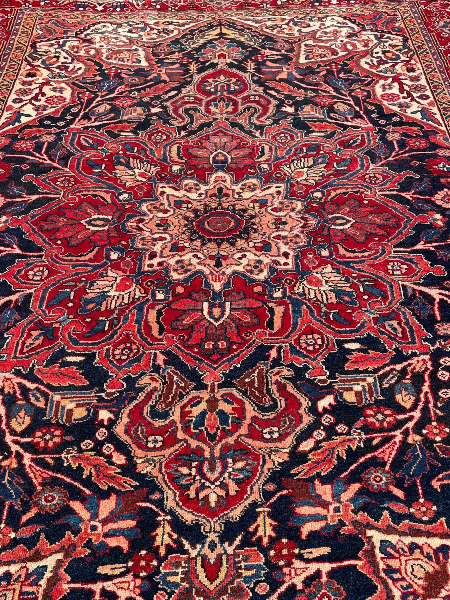 Persian Hamadan indigo and red ground carpet, large central medallion decorated with projecting palmette motifs, the surrounding field decorated with trailing branches and flower heads, crimson ground border decorated with stylised plant motifs, within floral pattern guard stripes 