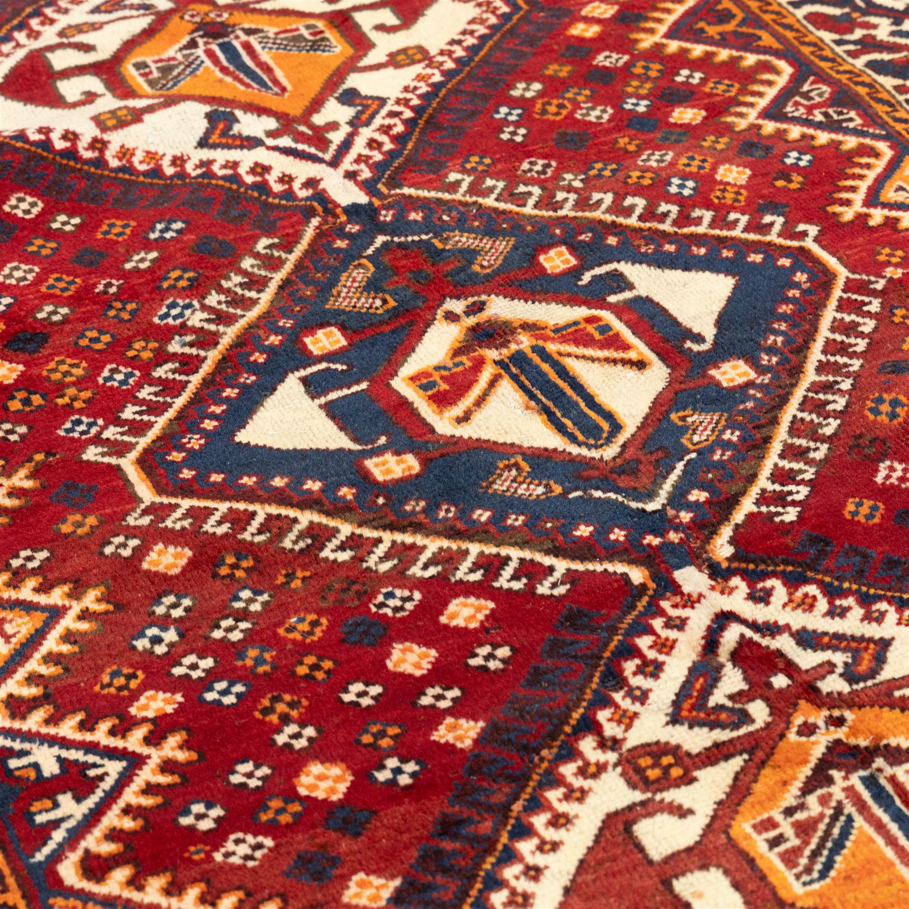 South West Persian Cori hand-knotted rug, red field with three central stepped lozenge medallions enclosing stylized geometric motifs surrounded by scattered rosette devices and angular ornaments within multiple geometric borders, with fringe ends  