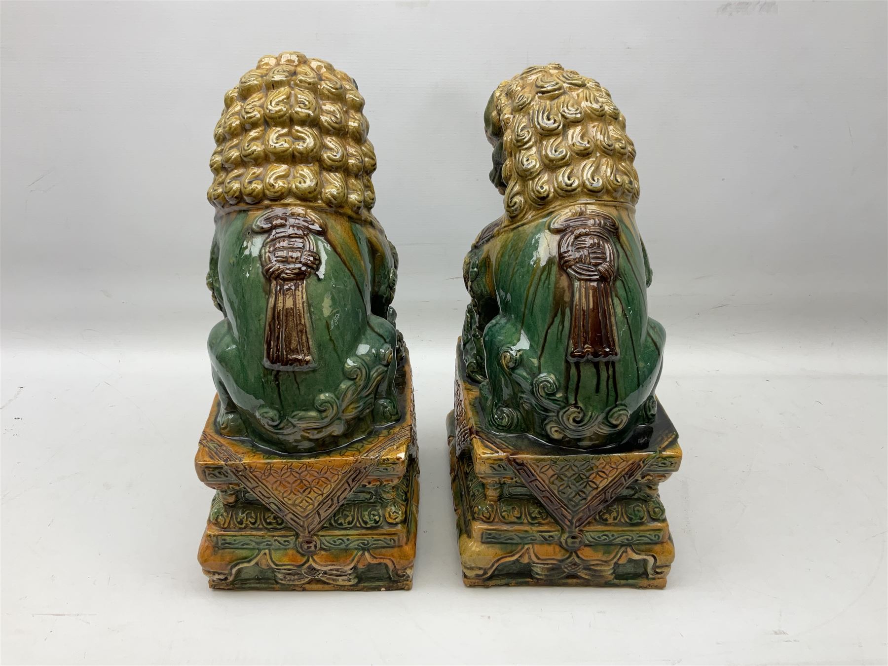 Pair of Chinese Temple Lions or Dogs of Foo, modelled in seated post, one with one front paw resting upon a ball, the other upon a cub, each upon stylised plinth base, H44cm