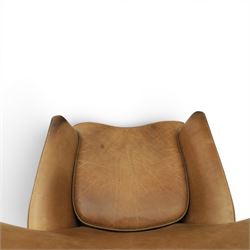 20th century tan leather armchair, the curved wing back above low square arms, shaped loose seat cushion with piped edge, close-nailed side detail, raised on concealed castors