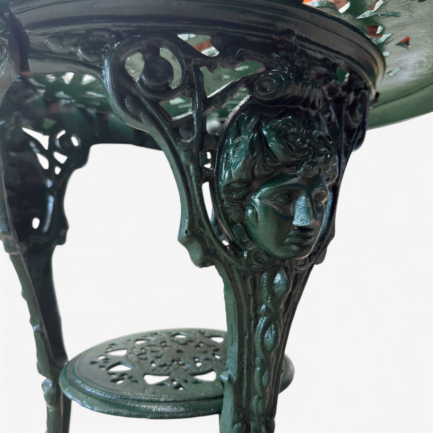 Painted cast iron garden table, the circular pierced top with foliate decoration and egg-and-dart rim, raised on three cloven hoof supports with classical female mask knees, united by pierced undertier, in green-painted finish