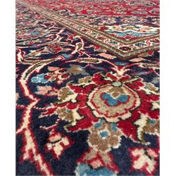 Central Persian Kashan hand-knotted carpet, the deep red ground with a central lozenge medallion in ivory and navy, surrounded by dense scrolling floral and vine motifs, navy spandrels and a wide border with stylised palmettes and flowerheads enclosed by multiple guard stripes