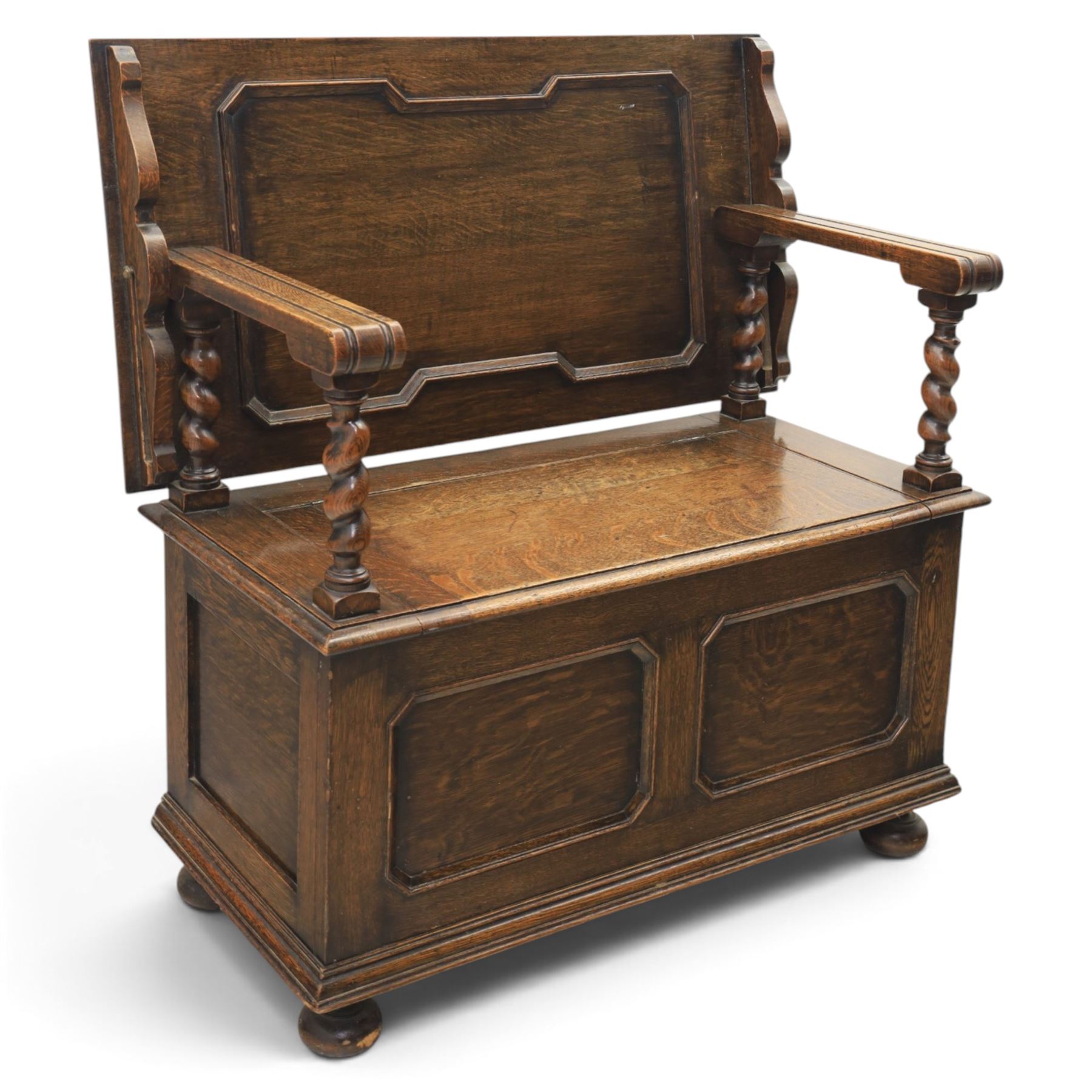 Early 20th century oak monks bench, panelled back converting to a table top, reeded armrests with barley twist uprights, hinged seat over panelled base supported on bun feet