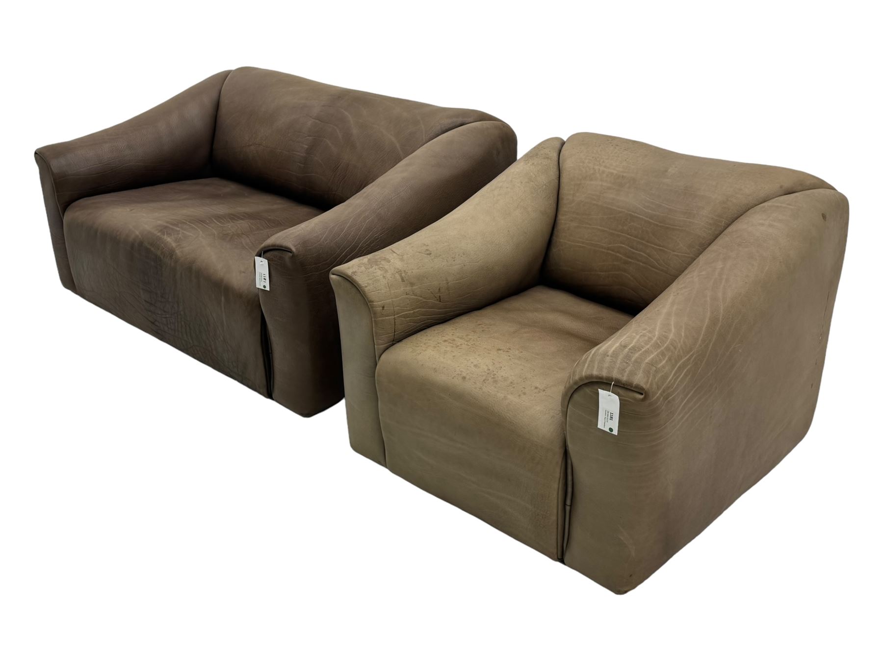 Mid-20th century two seater sofa, upholstered in soft brown leather with visible patina, curved arms and low back, on concealed supports (W138cm, D86cm, H72cm); matching armchair (W84cm, D86cm, H72cm)
