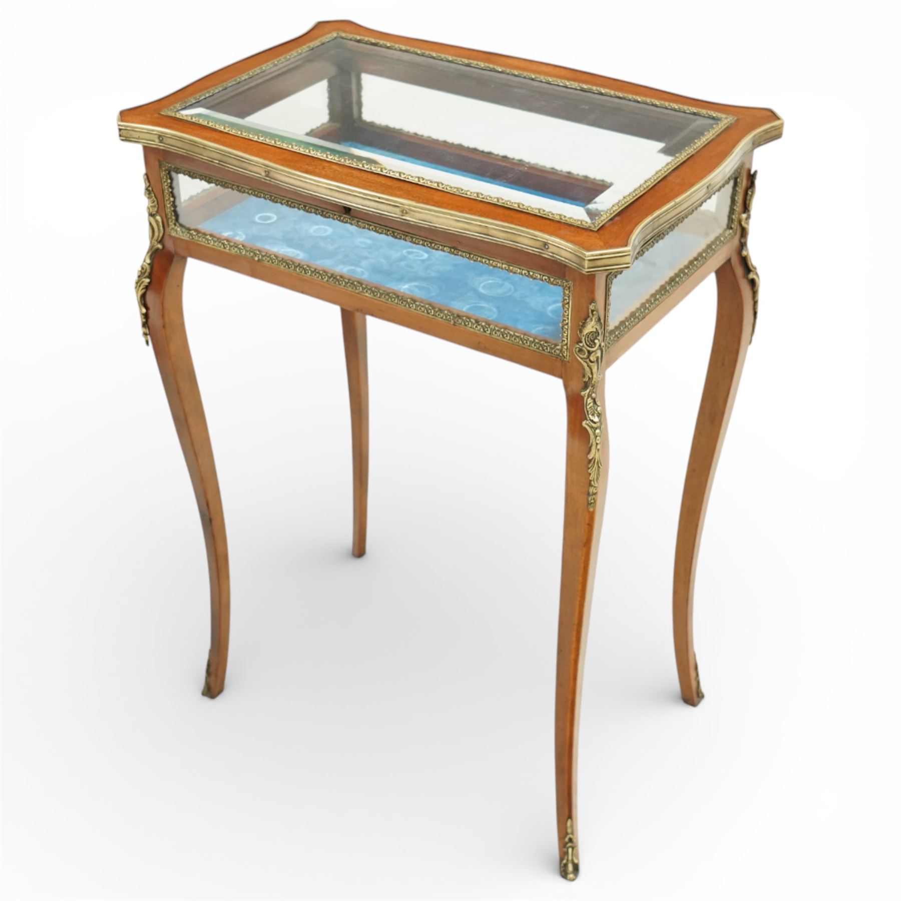Early 20th century French mahogany bijouterie table, the hinged shaped rectangular top with brass edge and gilt-metal foliate slip enclosing bevelled glass plate, raised on cabriole supports with applied gilt-metal cartouche and foliate mounts