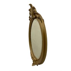 Victorian wall mirror, in oval moulded frame mounted by carved cartouches, bevelled glass plate