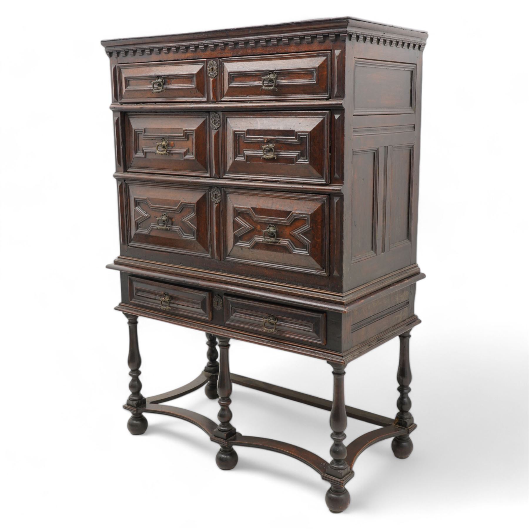 17th century oak chest on stand, moulded cornice over block work frieze, the upper section fitted with three long drawers each decorated with applied geometric mouldings and faceted panels, panelled sides with moulded frame, the stand fitted with two drawers, on five turned supports united by plan flat stretchers, terminating to turned feet