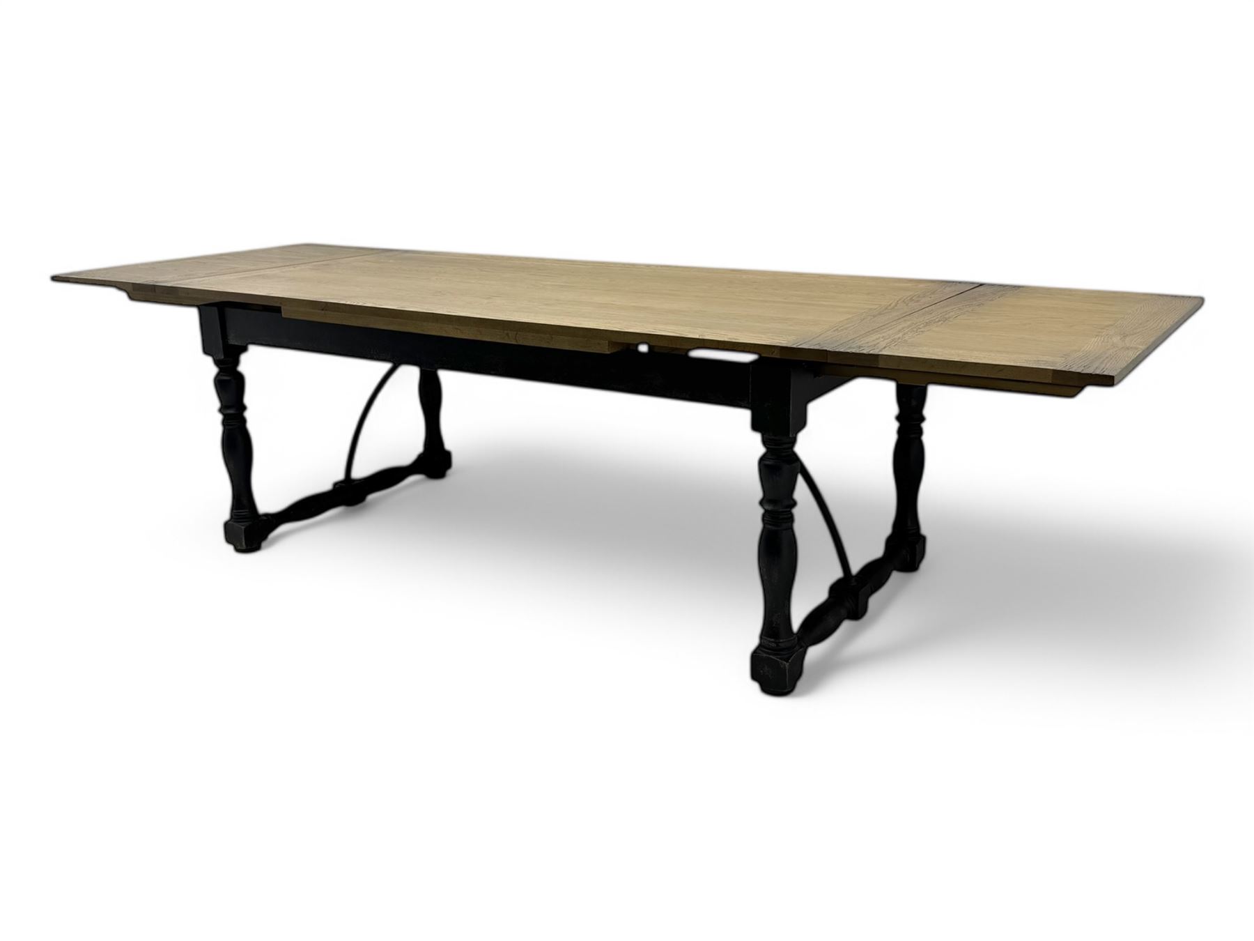 Barker & Stonehouse - large oak extending draw-leaf dining table, rectangular plank top over a black painted base, turned supports joined by shaped stretchers, extending at each end with pull-out leaves