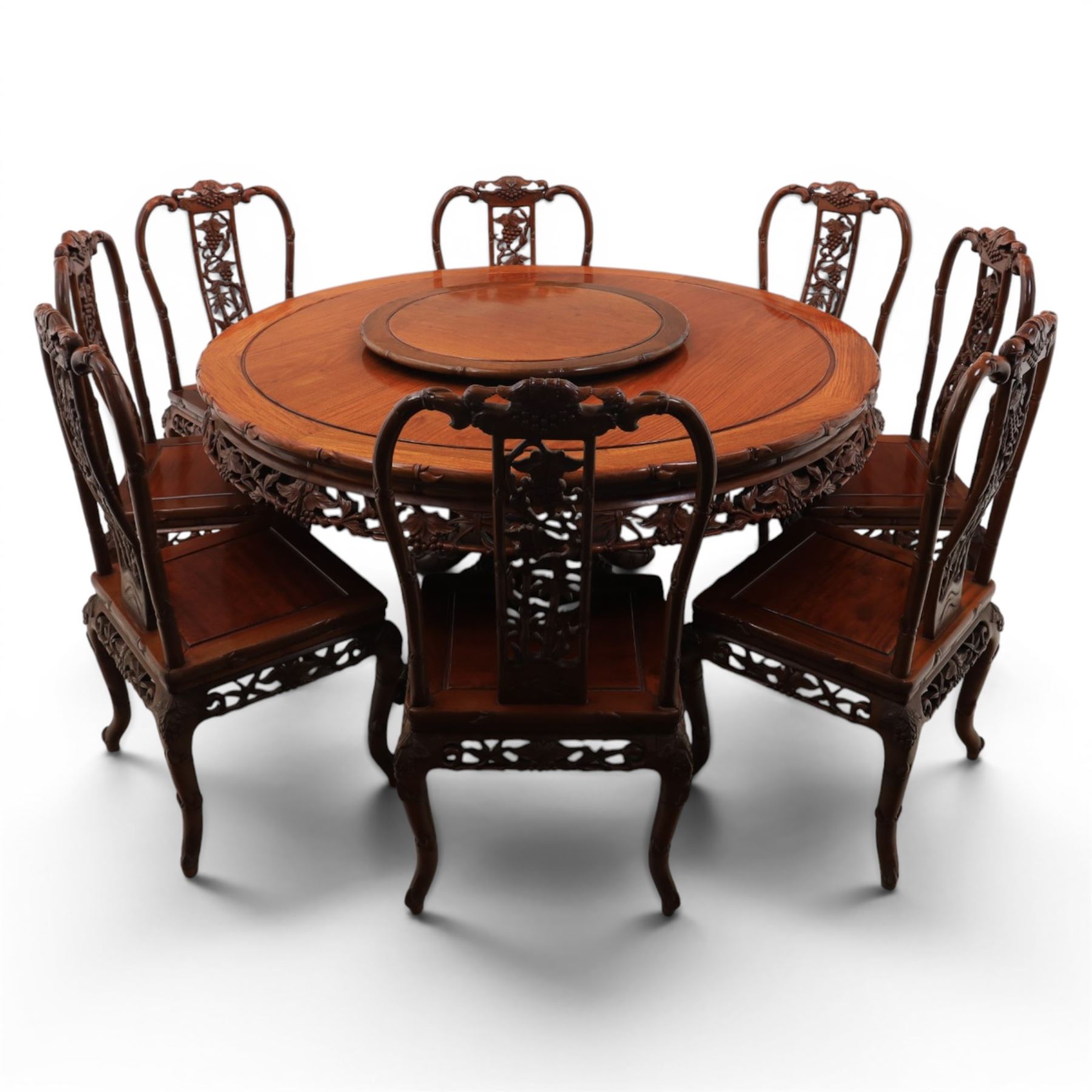 20th century Chinese ornately hardwood dining table and chairs, circular table with 'Lazy Susan' top with pierced carved frieze, raised on a quadriform base with carved foliate detail, the chairs en suite with carved pierced detailing  