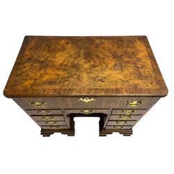 Early 18th century Queen Anne figured walnut kneehole desk with secretaire drawer, moulded and book matched top with walnut band, the top drawer with fall front enclosing small drawers and pigeon holes, fitted with nine drawers and central recessed cupboard, on ogee bracket feet
