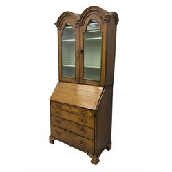 George III oak bookcase on bureau, the double arched top enclosed by two shaped glazed doors, fall-front concealing fitted interior, over four graduating cock-beaded drawers, on bracket feet