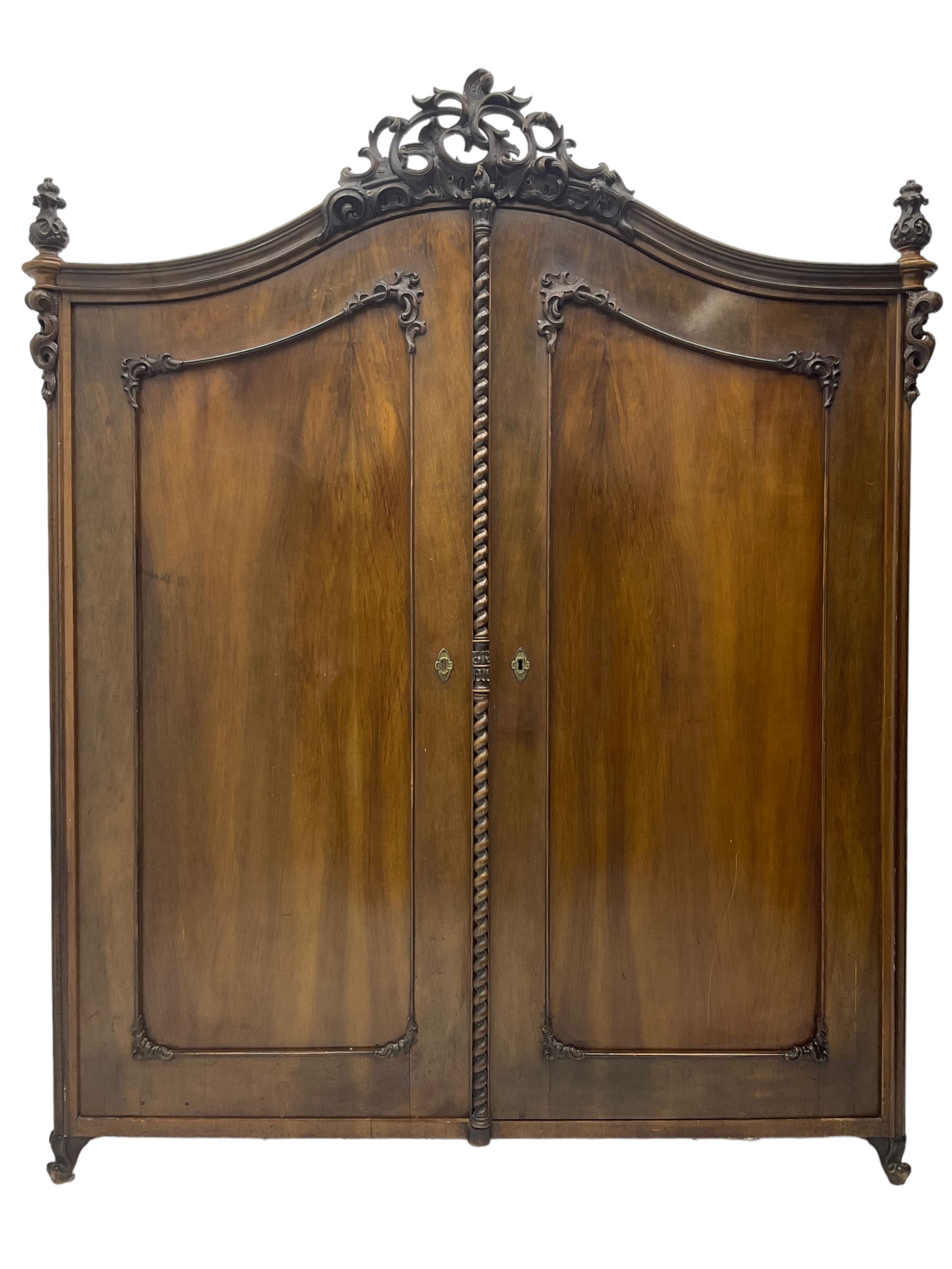 Early 20th century Italian walnut armoire wardrobe, the pierced and scrolling pediment carved with acanthus leaf detail, flanked by two scrolling cartouche with matching corbels below, the two panelled doors with applied carved rinceaux slips, with a central spiral turned upright, enclosing single shelf and hanging rail, raised on scroll feet