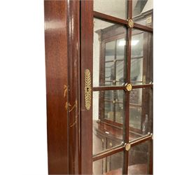 Pair of French Empire design corner cabinets, the straight-front upper section with canted corners and applied half-column pilasters, enclosed by mirror glazed door, the bow-front lower section enclosed by two doors with applied mouldings, mounted by cast metal floral rosettes, skirted base with cast gilt metal hairy paw brass feet