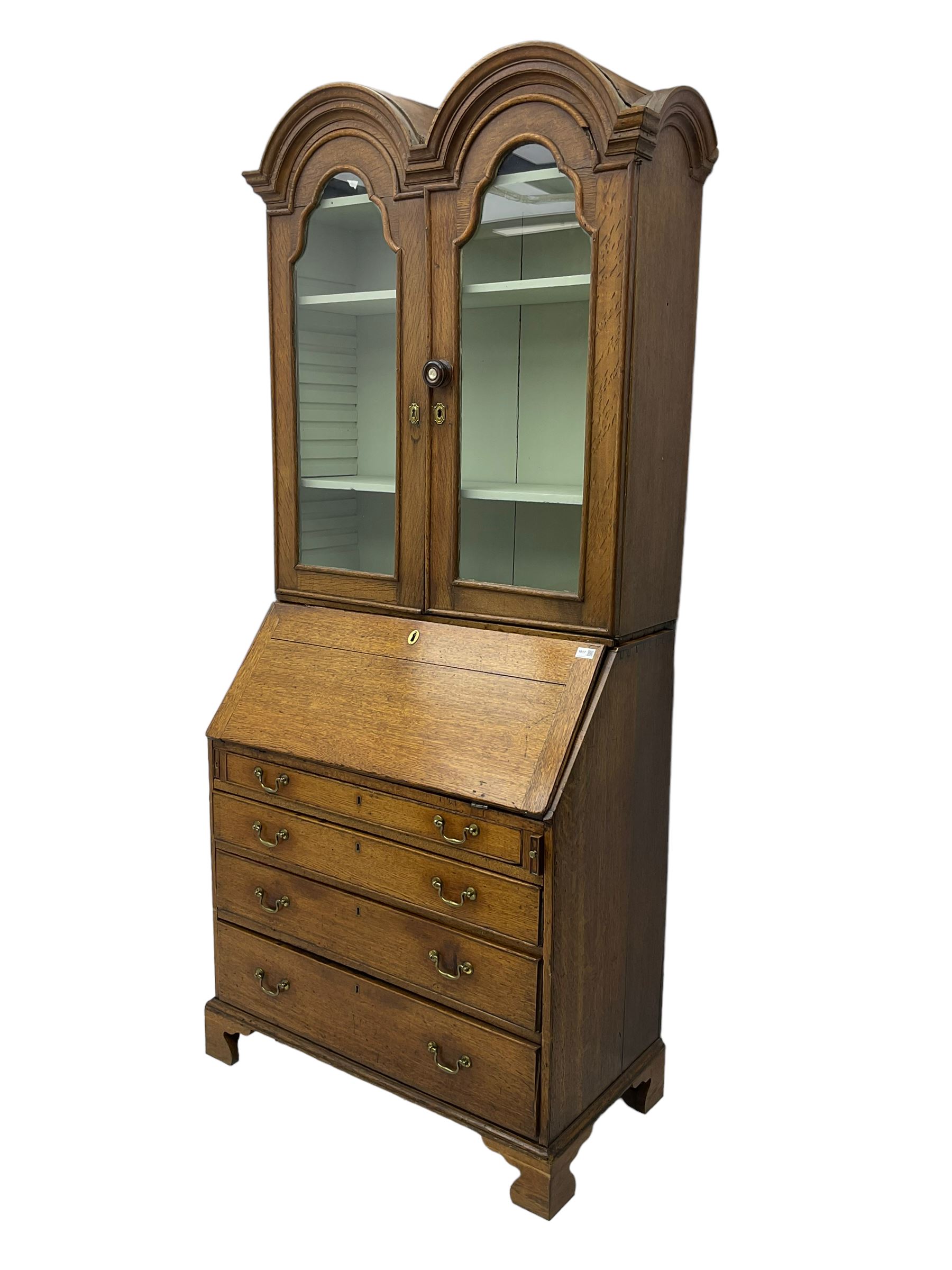 George III oak bookcase on bureau, the double arched top enclosed by two shaped glazed doors, fall-front concealing fitted interior, over four graduating cock-beaded drawers, on bracket feet