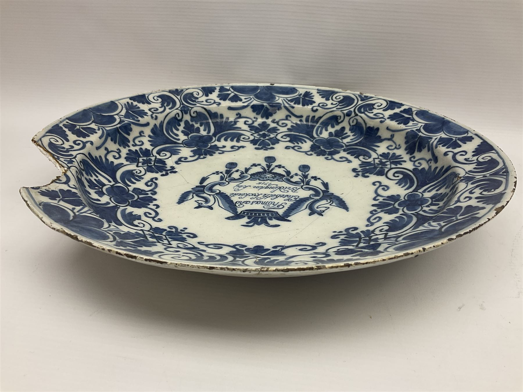 Early 18th century Delft marriage plate, of circular form with dished centre, the centre inscribed and dated 'Thomas and Elizabeth Kockerill Bridlington Key 1715' within a crowned C scroll cartouche, flanked by demi-griffins, above a putto head and tassels, within a wide foliate border, D34cm

