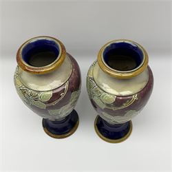 A pair of early 20th century Royal Doulton stoneware vases, of baluster form, decorated with roses and thorny vines against a mottled purple ground, with impressed marks and monogrammed for Florrie Jones beneath, H28cm. 